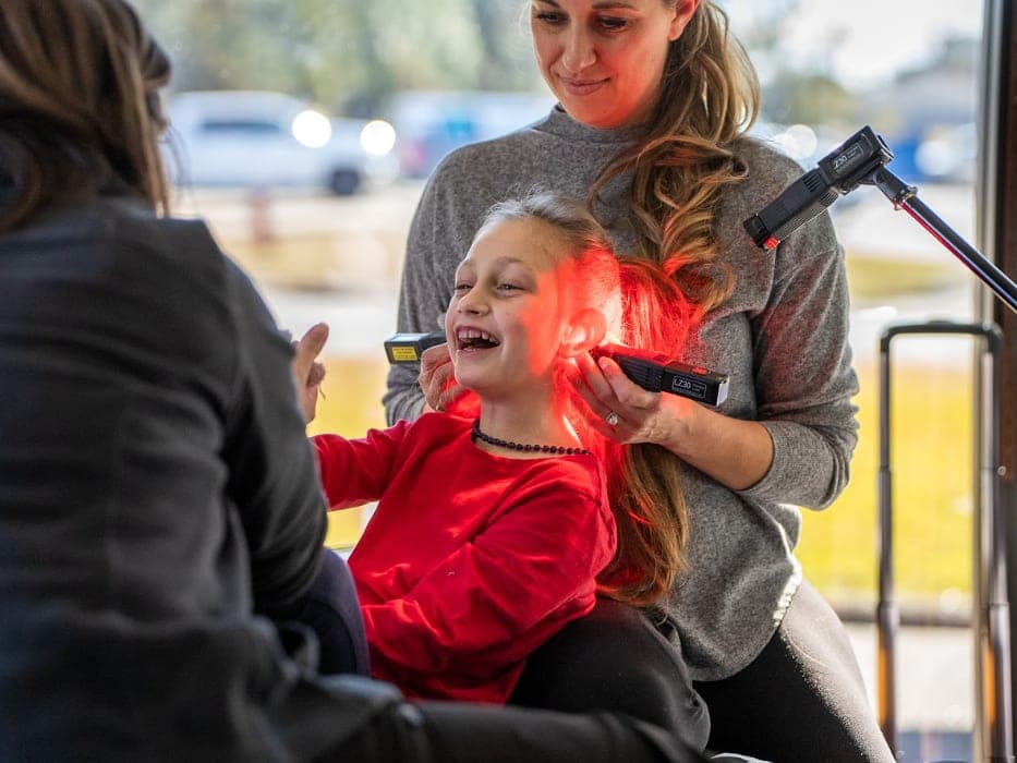 A child sits with a parent by a large window during a session with a clinician.