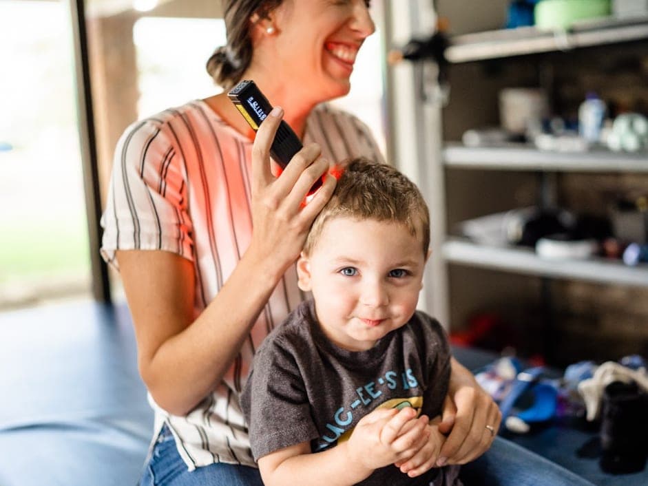 A parent sits with a child on a mat in a room lined with shelves.