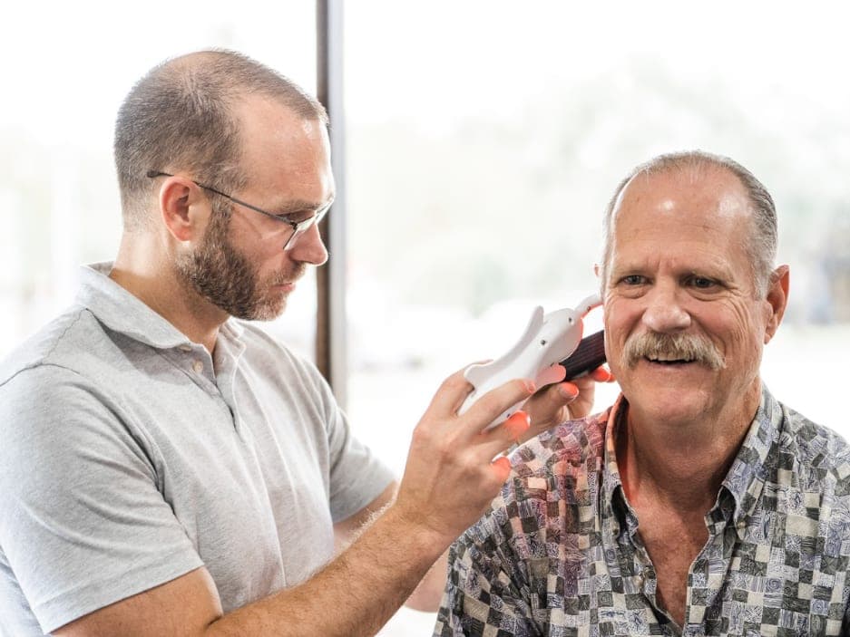 A clinician works beside an adult patient by a window.